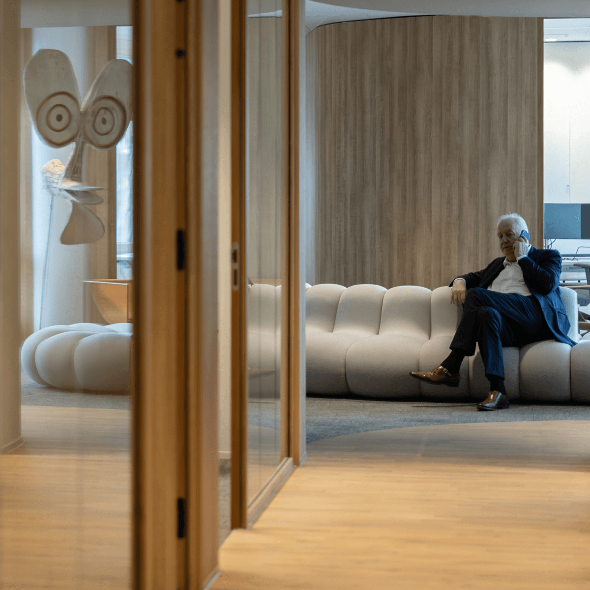 Zakenman in donker pak zittend op witte designbank en telefonerend HVK Stevens