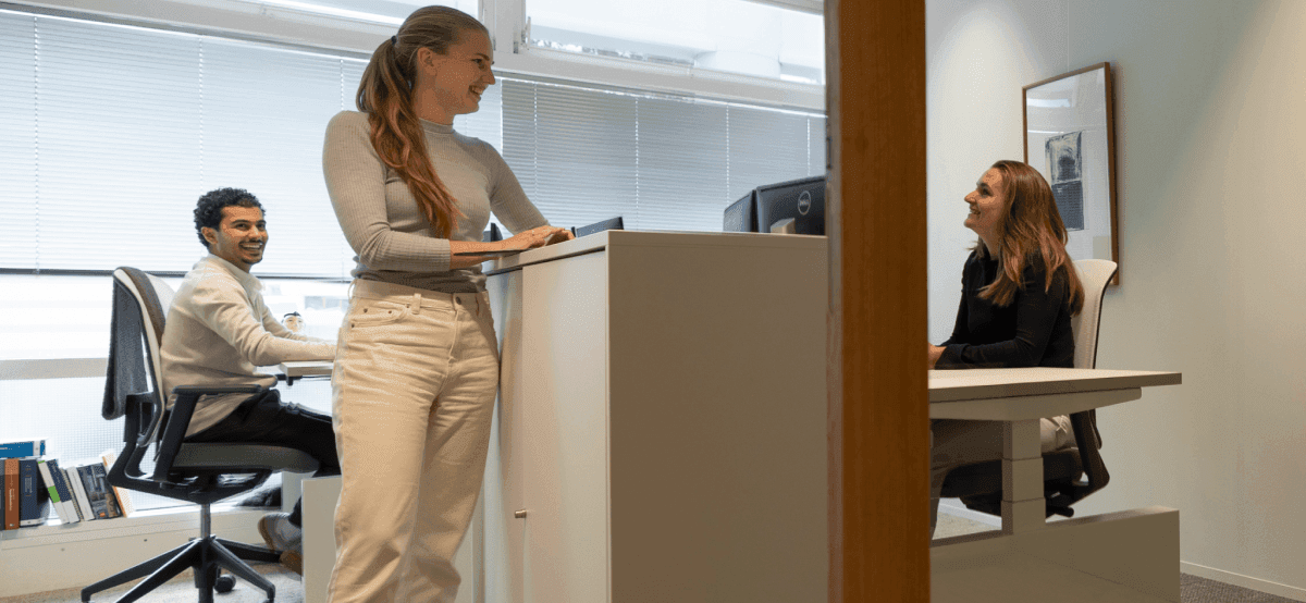 Drie collega’s lachend en overleggend in lichte kantoorruimte