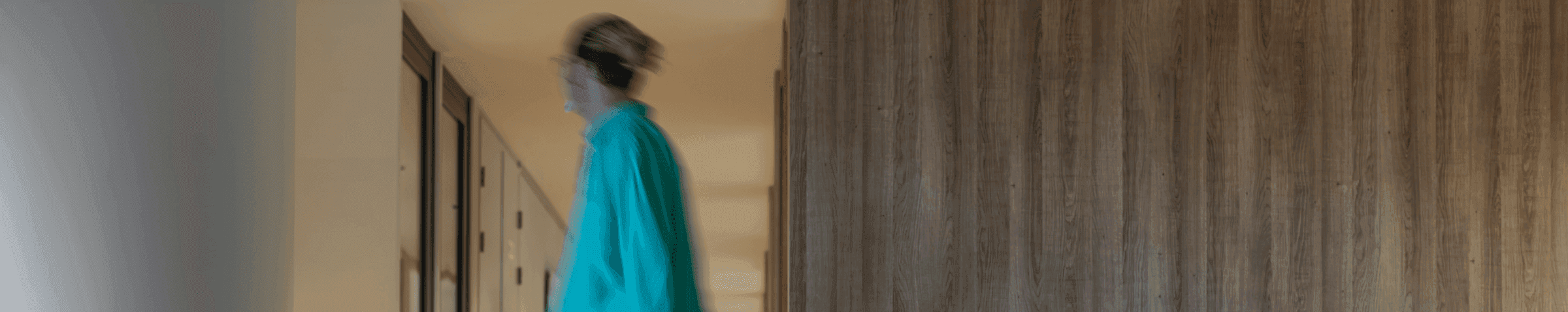 Person in green sweater walking through hallway with glass walls