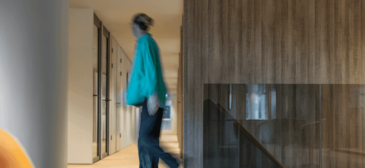 Person in green sweater walking through hallway with glass walls