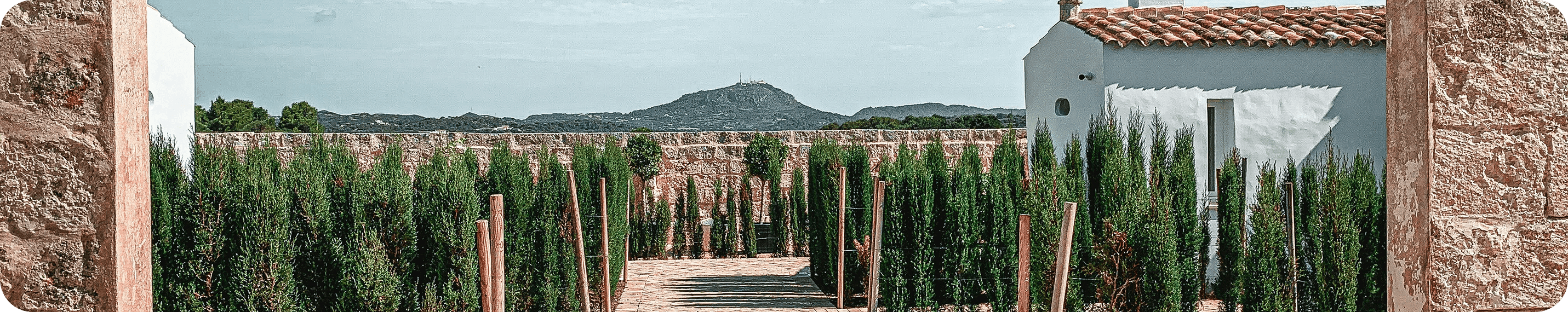 Mediterrane stenen tuin met cipressen, wit huis en uitzicht op de bergen