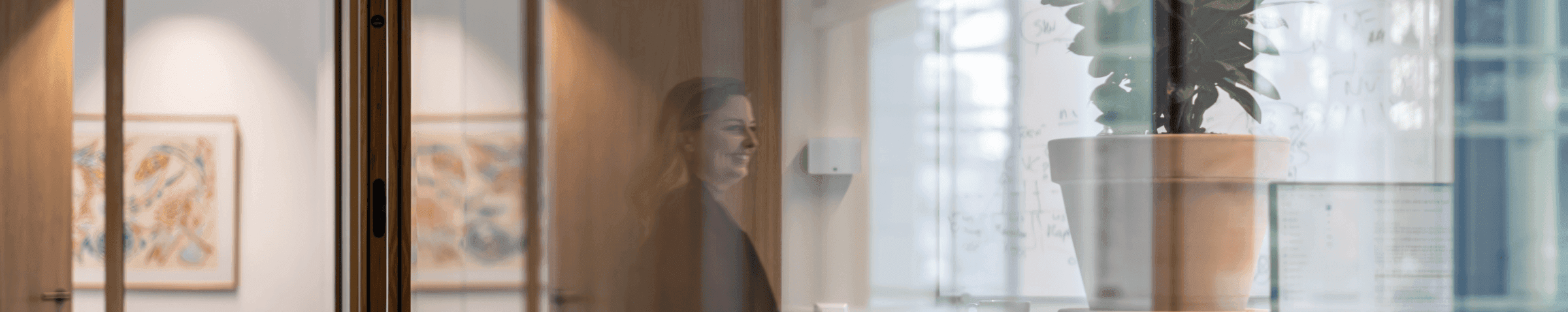 Woman visible through reflection next to whiteboard and plant